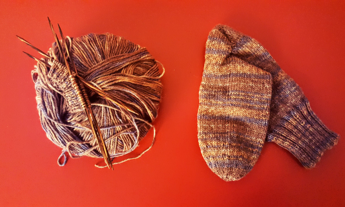 Ein Knäul Austermann Wolle liegt links von einem fertig gestrickten Socken